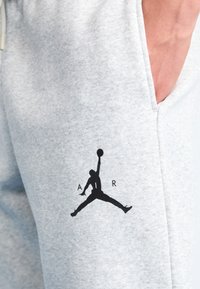 Grå sweatpants med en blød tekstur, der har et sort Jumpman-logo og 'A R'-bogstaver på venstre ben. Indeholder en sidelomme.
