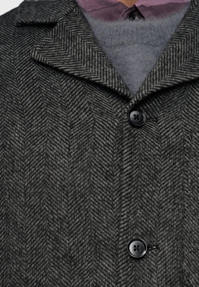 Παλτό με γκρι σχέδιο ψαροκόκκαλο, με γιακά με εγκοπές, τρία μαύρα κουμπιά και στρώση από γκρι πλεκτό ύφασμα από κάτω.