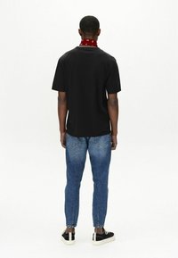 Tricou din bumbac negru cu decolteu rotund, combinat cu blugi din denim bleu deschis. Include o batic roșu legat în jurul gâtului și adidași negri.