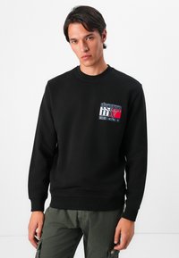 Zwarte sweatshirt met ronde hals, ribgebreide manchetten en zoom. Voorzien van een meerkleurig logo op de borst. Gladde textuur, casual ontwerp.