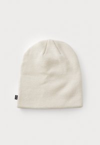 Knit beanie in off-white, featuring a soft texture, snug fit, and a small black brand tag on the side, with a rounded top.