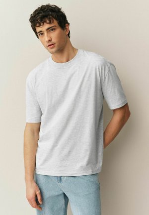 Grå t-shirt med korta ärmar i mjukt tyg, rund halsringning och avslappnad passform. Bärs med ljusblå jeans i denim. Mjuk textur.