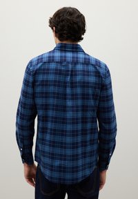 Navy plaid shirt with varying shades of blue, featuring a button-down collar, long sleeves, and a slightly curved hem.