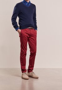 Mörkblå v-ringad tröja över en blå skjorta, parat med röda chinos och beige mockaskor. Inkluderar ett mönsterbälte. Avslappnad passform, mjuk textur.