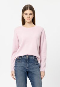 Hellrosa Pullover aus weichem Strickmaterial mit rundem Ausschnitt, überschnittenen Schultern und lockerem Schnitt, kombiniert mit hoch taillierten blauen Jeans.