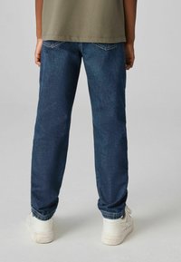 Jeans oscuros de corte relajado, con costuras en contraste y detalles en los bolsillos traseros, combinados con zapatillas blancas.