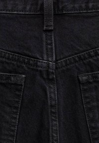 Gros plan sur un tissu en denim noir montrant les coutures de la poche arrière et le détail de la passants de ceinture.