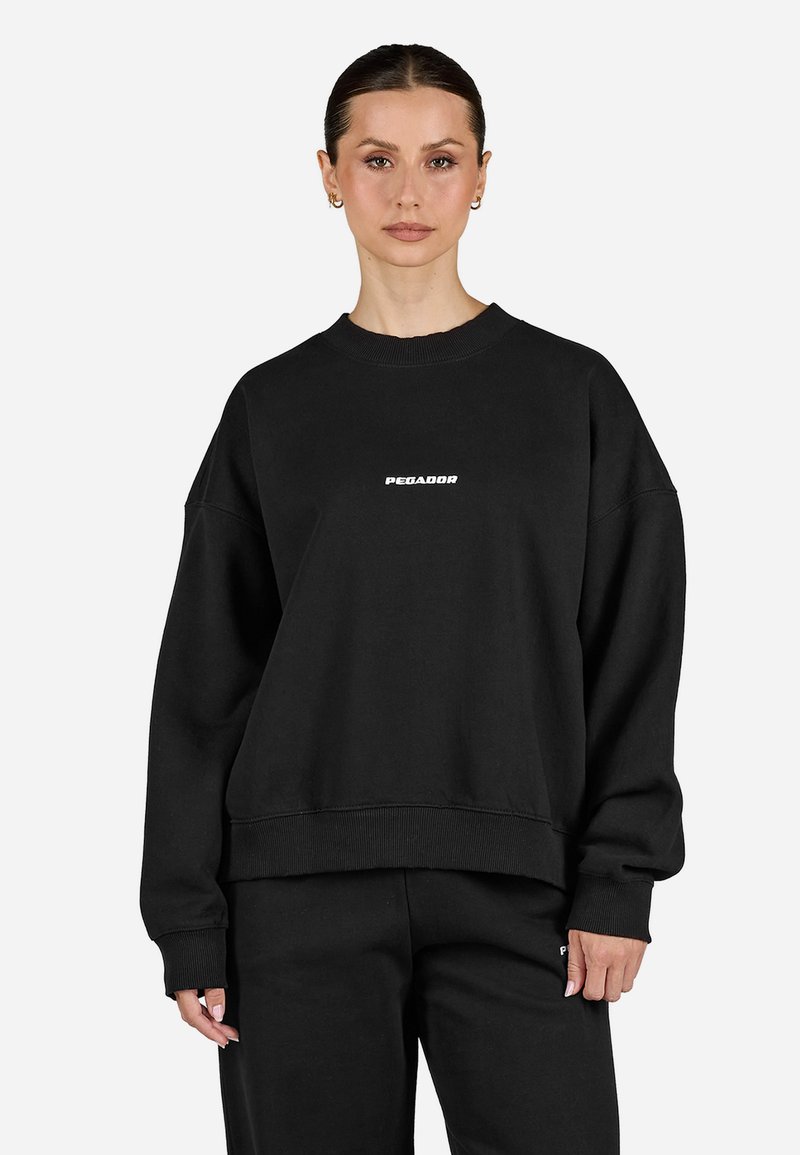 Sudadera negra de algodón con cuello redondo acanalado, hombros caídos y un logo blanco de "PEGADOR" en el pecho. Tejido texturizado.