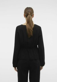 Top nero a maniche lunghe con scollatura arrotondata e vita aderente, realizzato in tessuto leggero, mostrato da dietro.