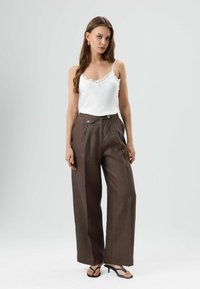 Witte kanten spaghettitop gecombineerd met hooggesneden, bruine wijde broek met twee knopen aan de voorkant en een gladde textuur.