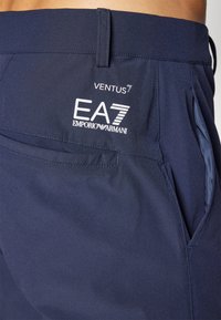 Shorts bleu marine en tissu léger avec une texture lisse, présentant une patch logo et des poches latérales. Conçus pour le confort avec une coupe moderne.