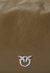 Bolsa de couro texturizado castanho com um detalhe em forma de pássaro prateado e ferragens circulares. A superfície apresenta um design ligeiramente pregueado.