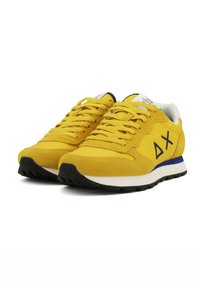 Sneakers in suede giallo con una intersuola bianca, suola nera e dettagli blu. Presentano lacci spessi e un logo geometrico sul lato.