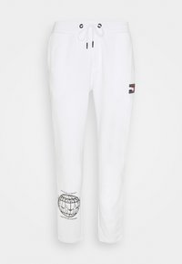 Vita sweatpants i mjukt tyg, med en logotypapplikation och en svart grafisk tryck med text på vänster ben. Dragsko i midjan.