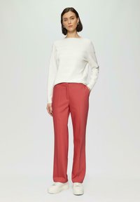 Biały sweter robiony na drutach z subtelnymi paskami, zestawiony z różowymi spodniami o wysokim stanie i białymi trampkami na platformie, tworząc nowoczesną stylizację.