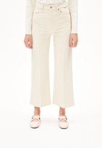 Wijd uitlopende, hoge crème jeans gemaakt van denim, met zakken en een knoopsluiting aan de voorkant. Gepaard met glanzende roze schoenen.