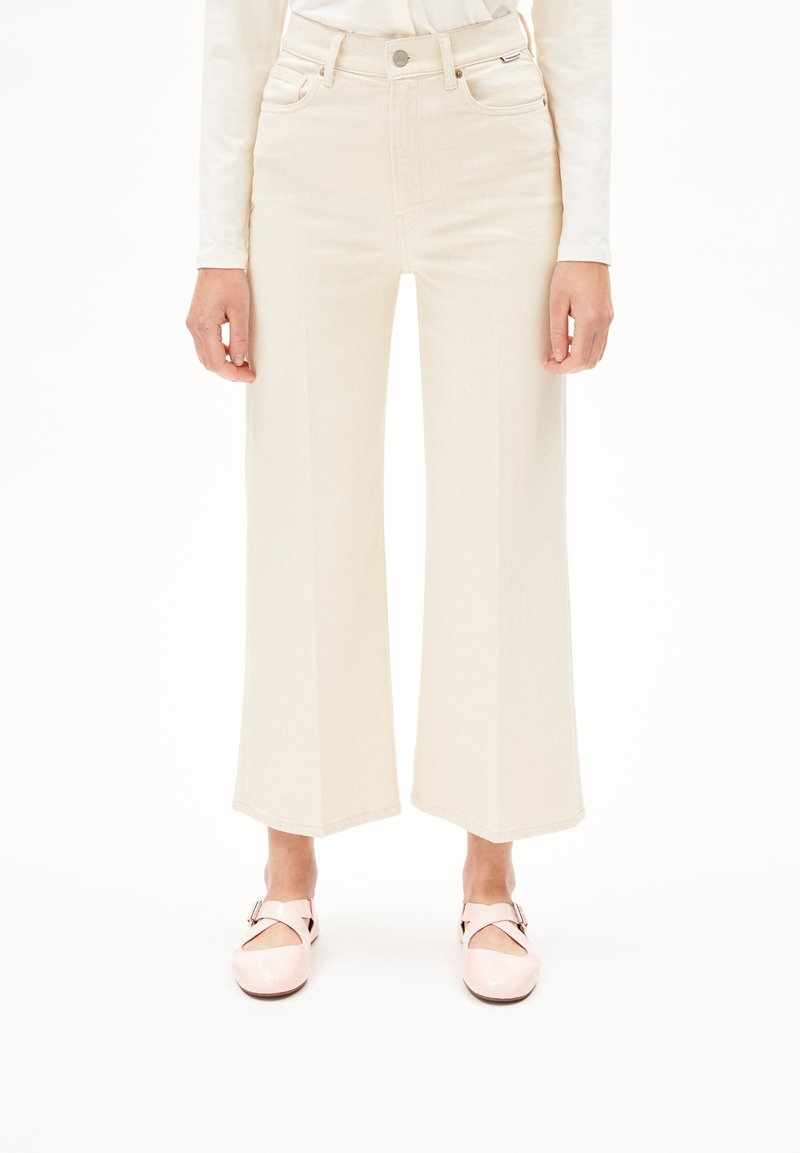 Wijd uitlopende, hoge crème jeans gemaakt van denim, met zakken en een knoopsluiting aan de voorkant. Gepaard met glanzende roze schoenen.