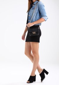 Czarna torebka na ramię z teksturowaną powierzchnią i złotymi okuciami, zestawiona z dopasowaną czarną spódnicą i denimową kurtką. Czarne, otwarte sandały na obcasie typu mule.