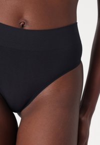Černé bikiny s vysokým pasem vyrobené z elastického materiálu, s hladkým povrchem a bez viditelných švů, navržené pro pohodlí a dokonalé padnutí.