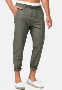 Luźne oliwkowe spodnie z elastycznym paskiem, podwiniętymi mankietami i gładką fakturą materiału. Noszone z białymi butami na slip-on.