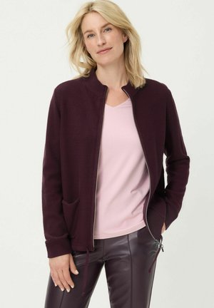 Weinroter Cardigan mit Reißverschluss, strukturiertem Strick, zwei Fronttaschen und einem Stehkragen über einem hellrosa V-Ausschnitt-Shirt.
