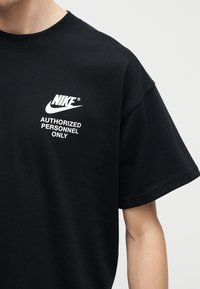 Άτομο που φοράει μαύρο T-shirt Nike με λευκό κείμενο "AUTHORIZED PERSONNEL ONLY" τυπωμένο στο στήθος.