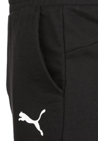 Schwarze Baumwoll-Jogger mit seitlichen Taschen, auf der Hüfte mit einem weißen Logo einer springenden Katze. Texturiertes Material und lockere Passform.