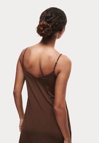 Abito marrone senza maniche con spalline sottili, tessuto liscio e silhouette aderente. Elementi di regolazione visibili sulle spalline.