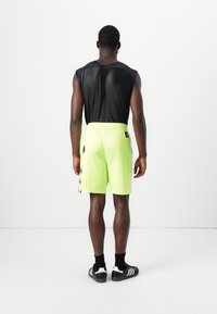 Čierny tielkový top, neónovo žlté šortky s čiernymi bočnými prúžkami, elastický pás a čierne športové topánky s bielymi pruhmi.