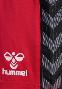 Rode stoffen korte broek met een wit "hummel" logo met een gestileerd ontwerp. De zijkant heeft een zwart gedeelte met witte zigzagpatronen.