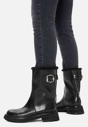 Czarne skórzane buty za kostkę z srebrnymi klamrami i zamkami z tyłu, noszone z dopasowanymi ciemnoszarymi dżinsami.