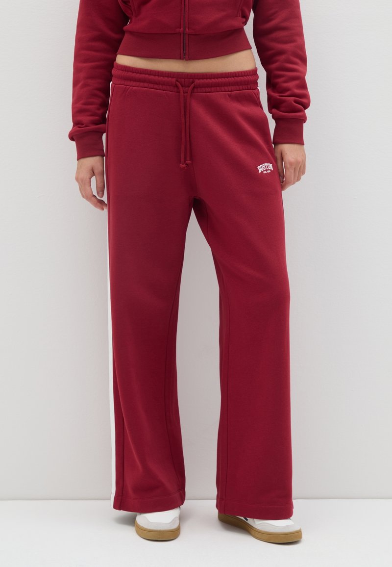 Pantalones de chándal burdeos en un corte relajado, elaborados con una tela suave. Presentan una cintura elástica con cordón y franjas blancas laterales.