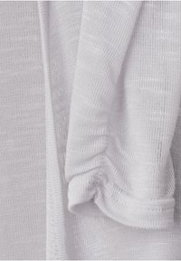 Närbild av ljusgrått stickat tyg med synliga texturer och veck som framhäver materialets mjuka och andningsbara egenskaper.