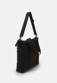 Saco de lona preto com formato retangular, featuring alças superiores duplas e uma alça de ombro ajustável. Textura suave e design minimalista.