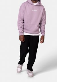 Hoodie oversize lilas avec poche avant, portant le texte blanc "crystal" ; associé à un pantalon noir côtelé et des baskets grises.