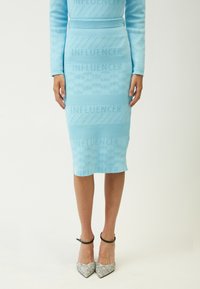 Hellblauer Strick-Bleistiftrock mit erhabenem "INFLUENCER"-Textmuster. Kombiniert mit glitzernden silbernen High Heels und schwarzen Knöchelriemen.