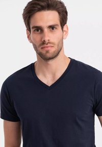 Námořnická modrá bavlněná tričko s výstřihem do V, krátkými rukávy a přiléhavým střihem, s hladkou texturou a minimálními detaily šití.