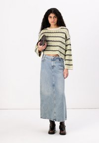 Strikket kort genser med grønne og svarte striper, kombinert med en lysvasket denim maxiskjørt og brune ankelstøvler, holder en liten veske.