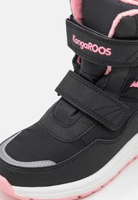 Baskets montantes KangaROOS noires et roses avec deux pattes Velcro, col rembourré et semelle blanche avec motif rose.