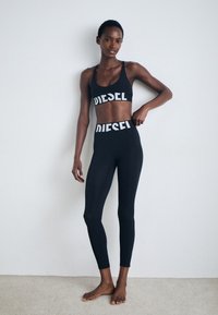 Tenue de sport noire comprenant un soutien-gorge de sport court et un legging taille haute, tous deux ornés de lettres blanches "DIESEL" bien visibles.