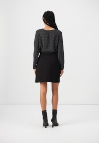 Jupe patineuse noire associée à un chemisier à manches longues noir et blanc moucheté, avec un col arrondi et une taille ajustée. Bottines noires.