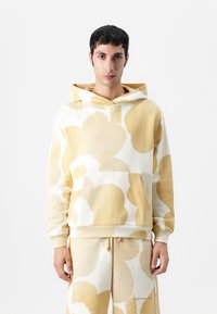 Hoodie mit Blumenmuster in Creme- und Gelbtönen, aus weichem Stoff gefertigt, mit einer Vorderentasche und gerippten Bündchen.