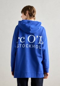 Blauer Hoodie mit lässiger Passform, großem Rückendruck "c O'D STOCKHOLM", gerippte Bündchen und Kapuze mit Kordelzug. Weiches Stoffgefühl.