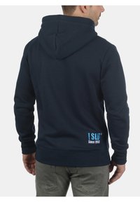 Marineblauer Hoodie aus Baumwollmix mit Kängurutasche und gerippten Bündchen. Mit gesticktem Logo in Hellblau auf dem unteren Rücken.