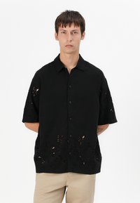 Μαύρο κοντομάνικο πουκάμισο με κομμένα λουλουδάτα σχέδια στο τελείωμα. Κατασκευασμένο από ελαφρύ ύφασμα. Διαθέτει γιακά και κουμπιά μπροστά.