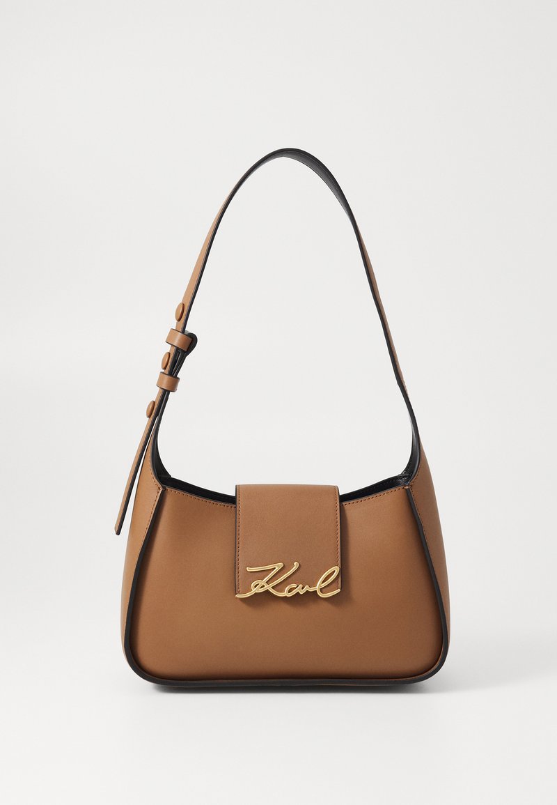 Καφέ δερμάτινη τσάντα χειρός με δομημένο σχήμα, που διαθέτει χρυσό λογότυπο και αποσπώμενο ιμάντα ώμου. Μαύρη περιφέρεια γύρω από τις άκρες.