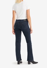 Mörk denim flare-jeans med midjehög passform, med en subtil slits vid ankeln och klassisk design på bakfickan. Kombinerad med en vit T-shirt.