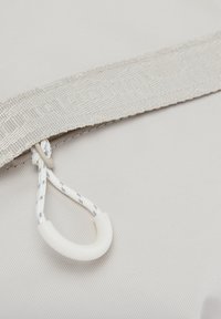 Weißer Stoffriemen mit eingewebtem Text und befestigter weißer Schlaufe, gesichert mit einem Kunststoffhaken vor hellem Hintergrund.