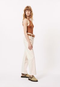 Débardeur marron à côtes, pantalon large crème avec une ceinture marron, et sabots verts à enfiler avec une semelle noire et une sangle ajustable.