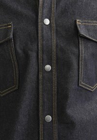 Camicia in denim scuro con bottoni a pressione argentati e cuciture gialle, dotata di tasche a toppa e una texture liscia.